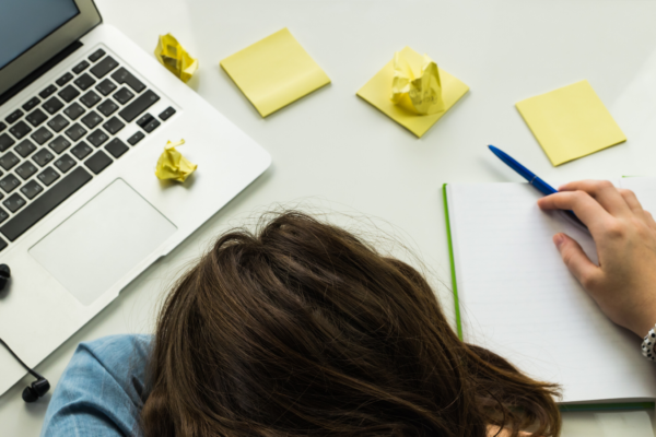 a woman experiencing burnout, lying on her desk in stress